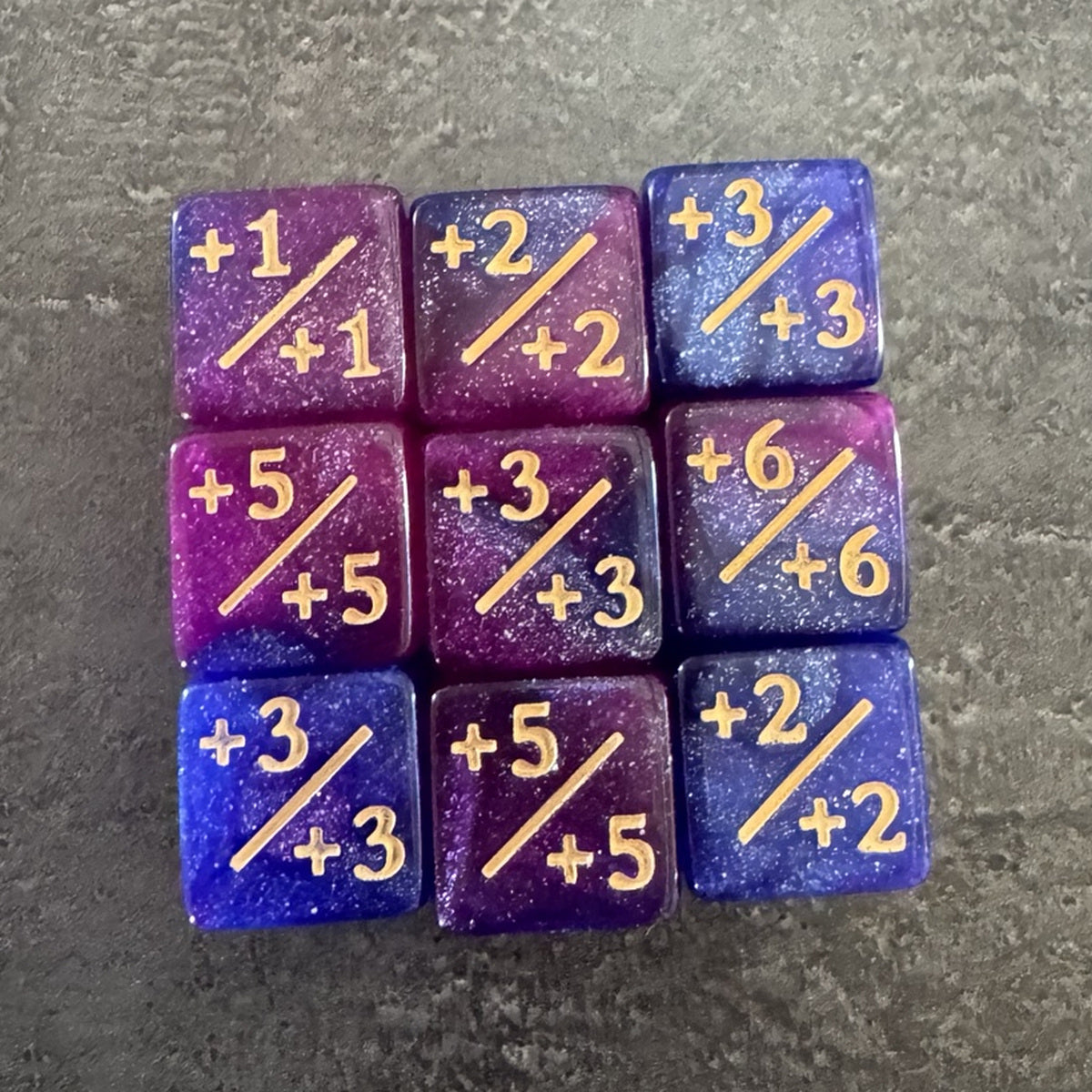 Photo réelle recadrée : 9 dés compteurs positifs rose, violet et bleu pailletés. / Cropped original photo: 9 pink, purple and blue glitter positive counter dice.