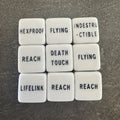 Photo réelle recadrée : 9 dés blancs de capacités à mots-clés anglais. / Cropped original photo: 9 white keyword dice with black English text.