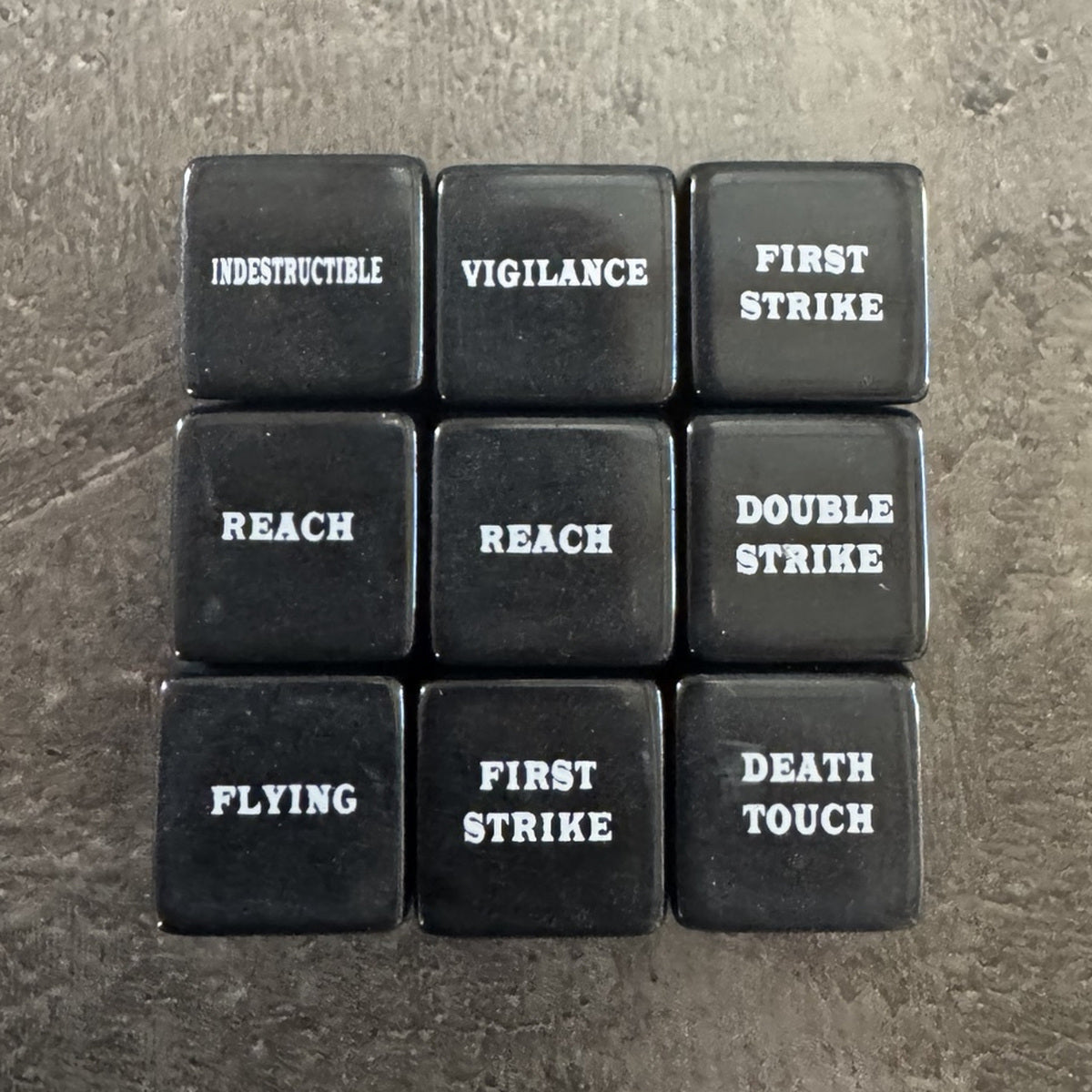 Lot de 9 dés noirs de capacités avec texte blanc en anglais, dont Deathtouch. / Set of 9 black keyword dice with white English text, including Deathtouch.