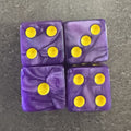Photo réelle recadrée : 4 dés violets nacrés à points jaune doré. / Cropped original photo: 4 pearlescent purple D6 dice with yellow-gold pips.