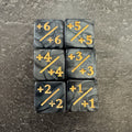 Lot de 6 dés compteurs positifs noirs et gris marbrés, marquages dorés +X/+X. / Set of 6 marbled black and grey positive counter dice with gold-coloured markings.